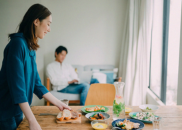 キッチンで料理をする女性とリビングでくつろぐ男性。家族が自然体で過ごせる平屋の家
